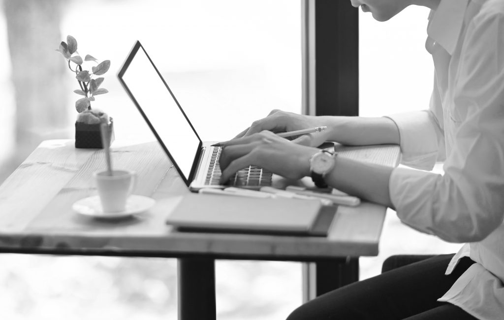 Cropped image of smart man working with white blank screen computer laptop while sitting at the wooden working desk over modern office as background.